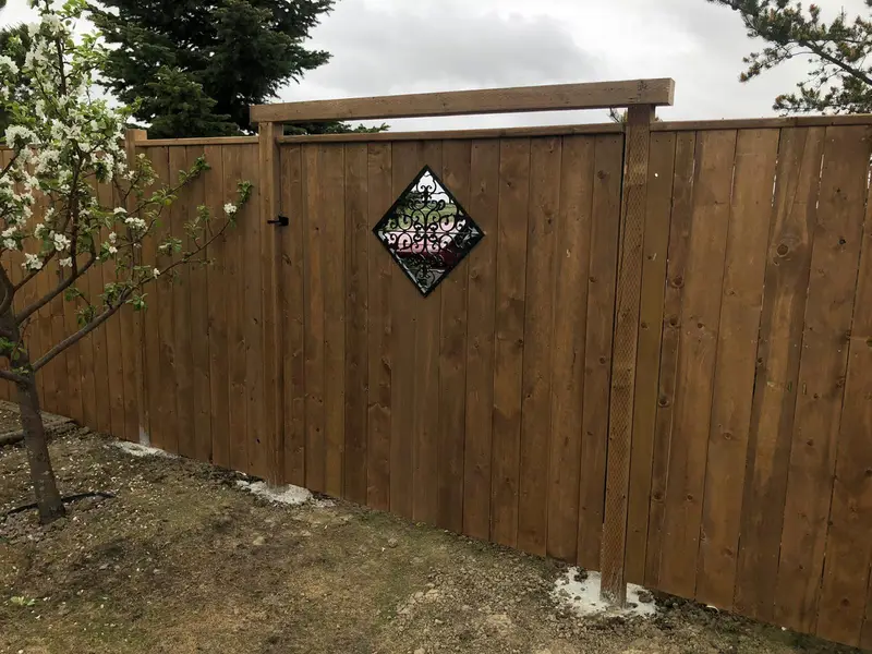Wood Privacy Fence with Decorative Accent Stained wood privacy fence with a decorative wrought-iron diamond inlay and an arched post beam in Saskatoon