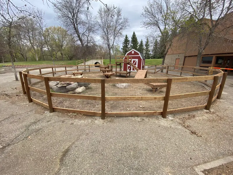 Rail & Wire Mesh Enclosure Fence Curved wood rail fence with wire-mesh infill enclosing a fire-pit gathering area near a red barn